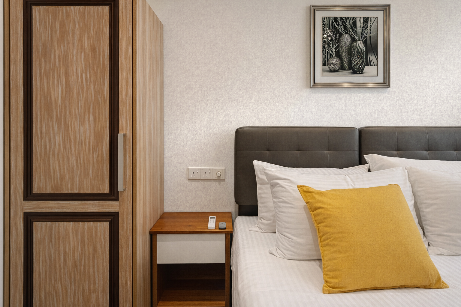 Modern bedroom featuring a bed with a yellow accent pillow, wooden wardrobe, and bedside table